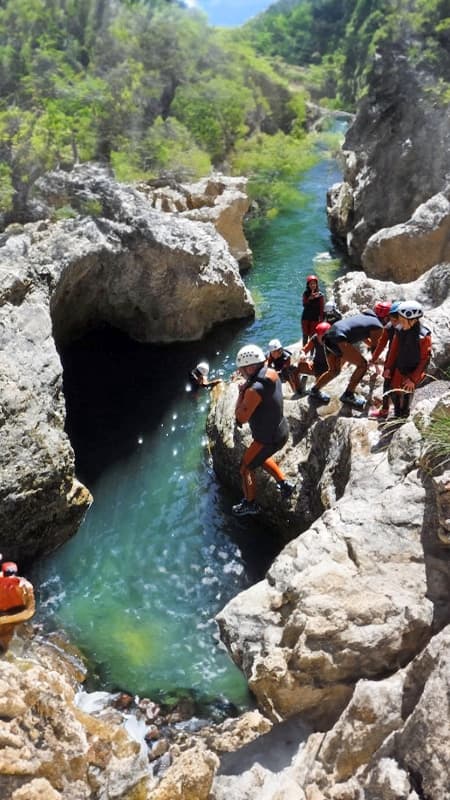 Group of people in wetsuits and helmets preparing for a jump in the Río Blanco Canyon, Pyrenees.