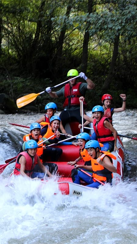 Group of people with helmets and life jackets paddling a rafting boat through the rapids of the Noguera Ribagorçana River.