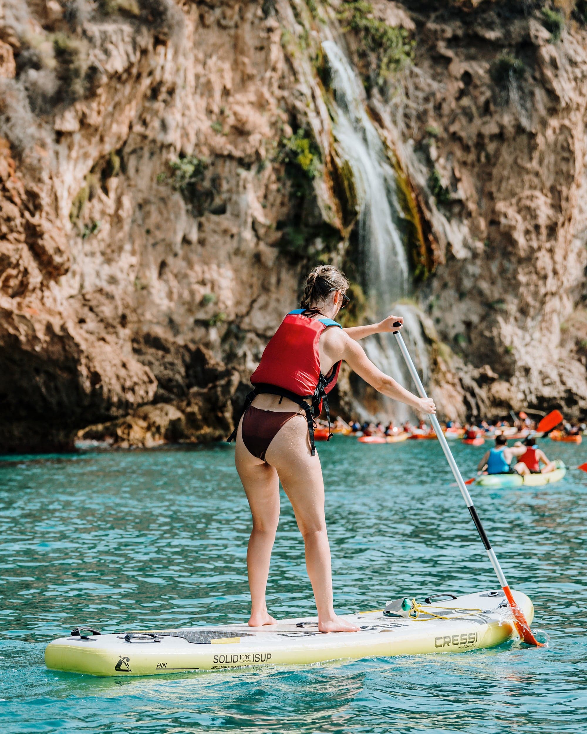 Person paddle surfing in front of the Maro Waterfall at the Nerja cliffs.