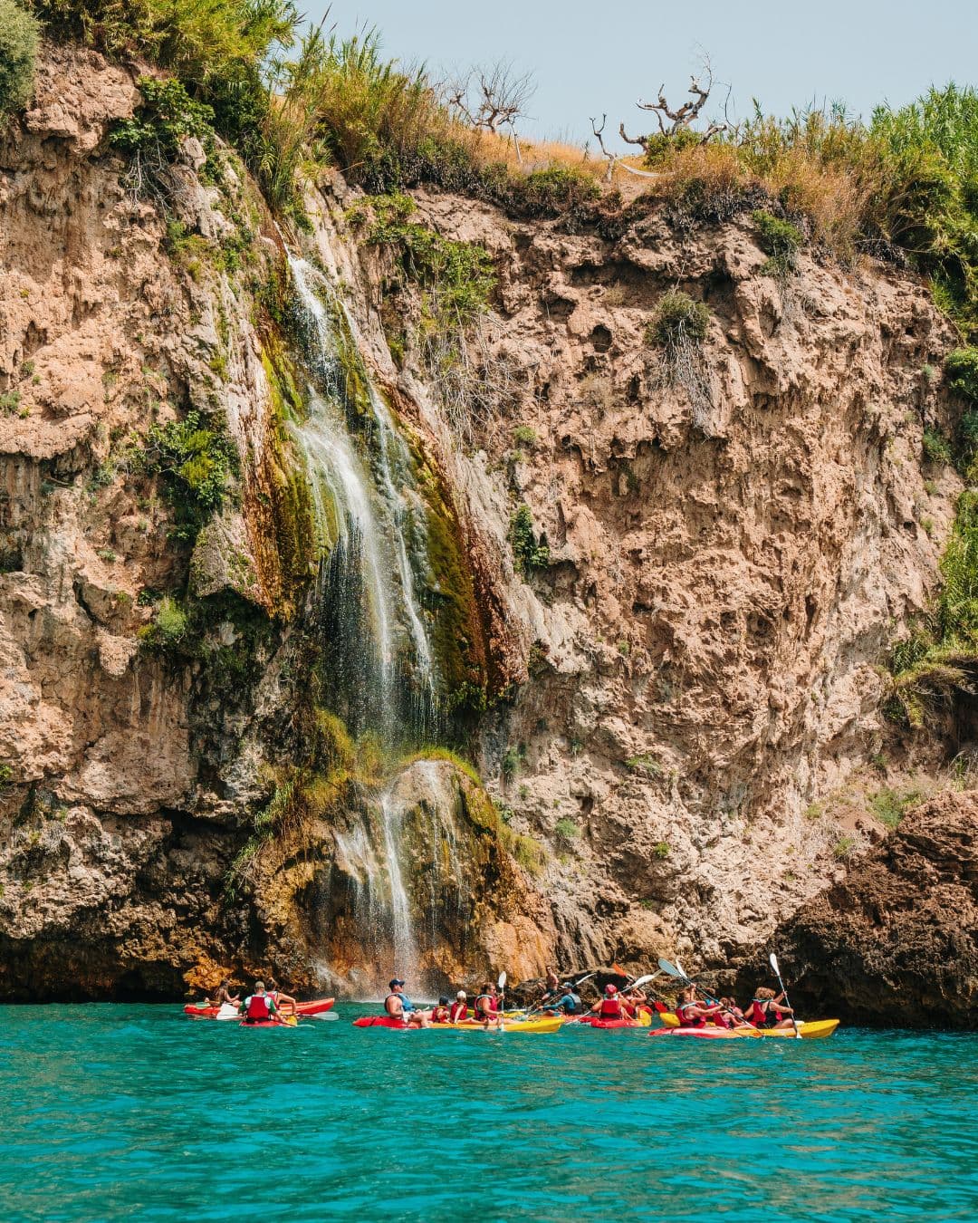 Group of people in kayaks paddling near the Maro Waterfall at the Nerja cliffs.