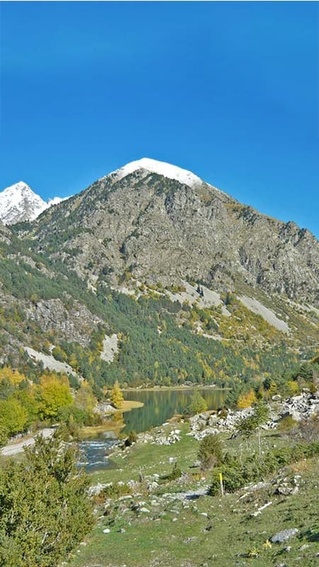 Hikers walking on a high mountain trail overlooking the meanders of Aigüestortes National Park.