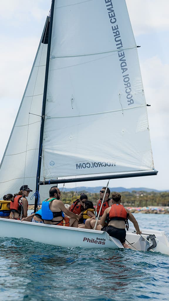 Sailing instructor teaching a small group how to handle the sheet on a group sailboat off the Garraf coast.